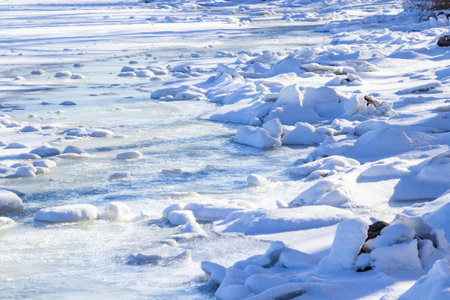 Pieces of ice covered with snow on the river bank. Frozen river.