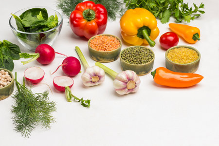 Cereals, vegetables and greens on table. Mash, lentils, bulgur in bowls. Radish halves, garlic and colored peppers. White background. Top view. Copy spaceの写真素材
