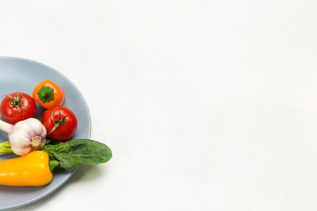 Yellow peppers, garlic and red tomatoes on gray plate. Cucumbers and peppers in gray mesh. White background. Top viewの写真素材