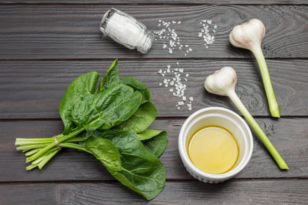 Spinach leaves are tied in bunch. Olive oil in white bowl. Garlic and salt on the table. Dark wooden background. Flat lay.の写真素材