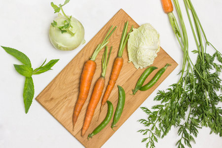 Spring carrots, green peas and savoy cabbage on cutting board. Kohlrabi, lime and carrot tops on...