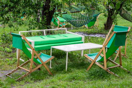 Folding wooden chairs, a summer sofa and a table on a lawn in the garden. Recreation area in the park.の写真素材