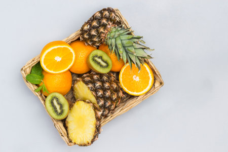 Pineapple, orange and kiwi sliced in rattan basket. . Gray background. Flat layの写真素材