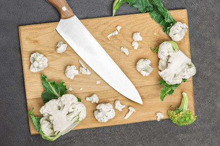 Kitchen knife, fresh cauliflower and broccoli on cutting board. Broccoli cabbage leaves. Black background. Flat layの写真素材