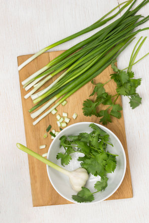 Cilantro and garlic in white bowl. Green onions on cutting board. Dill on table. White background. Flat layの写真素材