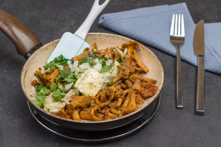 Fried chanterelles in pan. Fork and knife on gray napkin. Black background. Top viewの写真素材