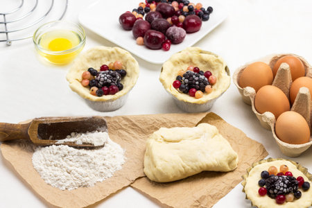 Making cake from frozen berries. Flour and dough on paper. Dough and berries in baking cup. White...