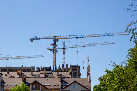 Roofs of houses and construction cranes against the blue sky.の写真素材