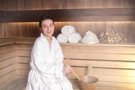 Beautiful young woman in a white coat is relaxing in a saunaの写真素材