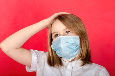 portrait of young illness girl with closed eyes, wearing medical flu mask, holding her head with hand, isolated on red backgroundの写真素材
