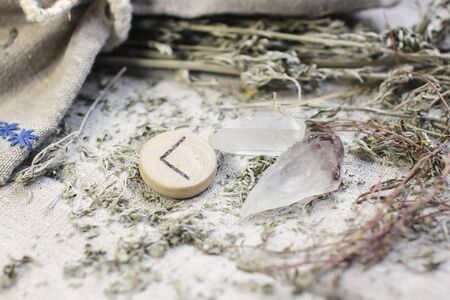 Scandinavian wooden rune Kauna, Kenaz on a rough linen cloth with amethyst crystalline, rock crystal and dried wormwood.の写真素材
