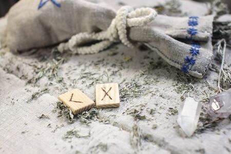 Scandinavian wooden rune Kenaz and Gebo on a rough linen cloth with amethyst crystalline, rock crystal and dried wormwood.の写真素材