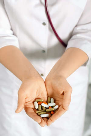 Woman in white coat holding a handful of pills in palmsの写真素材