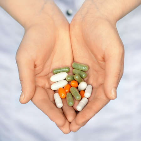 Woman in white coat holding a handful of pills in palmsの写真素材
