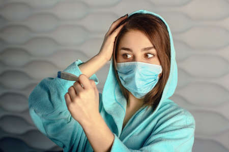 young woman in a mask holding a thermometerの写真素材
