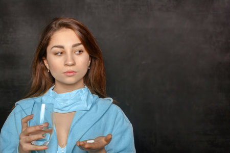 young woman on a black background holding a pill and a glass of water in her handsの写真素材