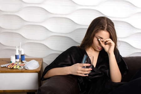 a young woman is ill at home, she holds a pill and a glass of water in her handの写真素材