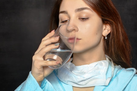 Young woman in a blue terry dressing gown drinks water from a glassの写真素材