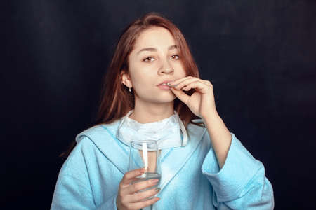 young woman on a black background holding a pill and a glass of water in her handsの写真素材