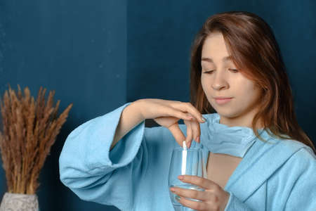 young woman on a black background holding a pill and a glass of water in her handsの写真素材