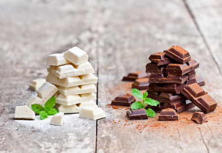 Piles  of white and dark chocolate slices with mint on an old wooden table.の写真素材