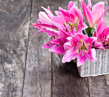 White  basket with pink lily flowers bouquet on rustic wooden tableの写真素材