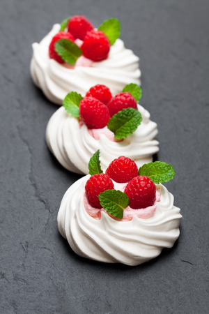 Mini  Pavlova meringue nests with raspberries and mint on black stone background の写真素材