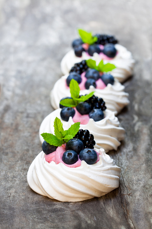 Mini  Pavlova meringue nests with berries and thyme on rustic wooden table の写真素材