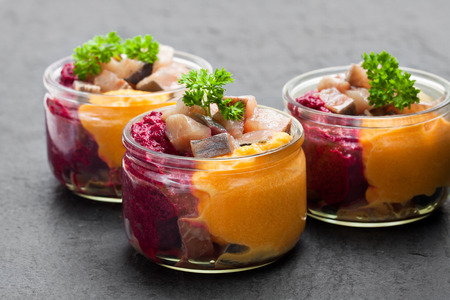Herring  salad with colorful vegetables in a small glass jars on black stone backgroundの写真素材