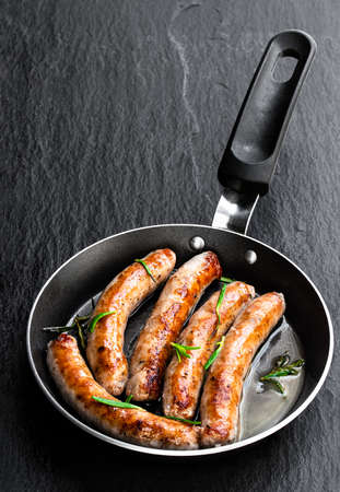 Delicious pork chipolatas sausages in a frying pan on black stone backgroundの写真素材