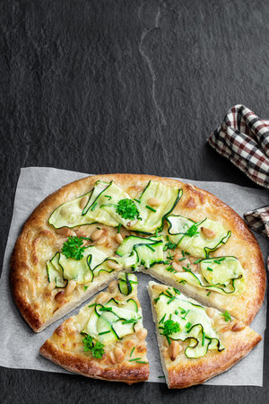 Vegetarian pizza with zucchini and pine nuts on black stone background