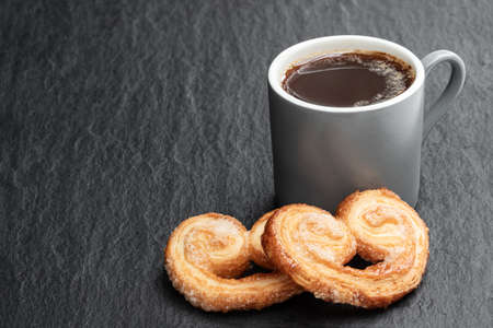 Flaky pastry hearts glazed with caramelized sugar and cup of coffee on black stone backgroundの写真素材