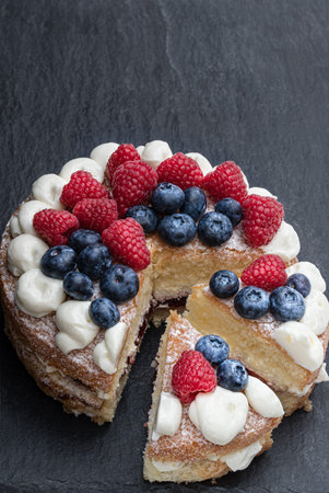 Victoria  sponge cake with whipped cream and berries on top on stone background