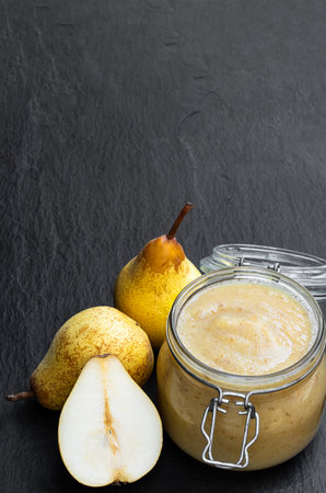 Homemade  pear puree in glass jar with fresh ripe pears on black stone backgroundの写真素材