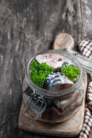 Mackerel  in brine with onion and spices in glass jar on wooden tableの写真素材