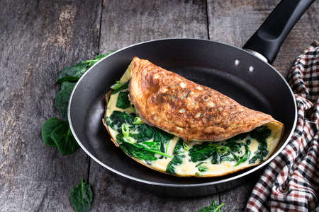 Omelette with spinach and cheese in a pan on wooden tableの写真素材