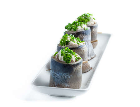 Appetizing  pickled herring rolls stuffed with cream cheese and egg mass served on wooden board isolated on whiteの写真素材