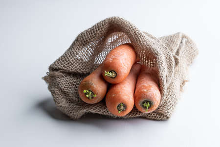 Carrots in a burlap bag on white wooden tableの写真素材