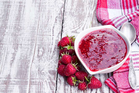 Raspberry jam in porcelain saucer on white wooden tableの写真素材