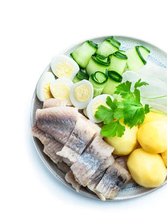 Salted herring with boiled potatoes and quial eggs on a white plate isolated on whiteの写真素材