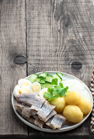 Salted herring with boiled potatoes and quial eggs on a white plate on wooden tableの写真素材