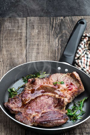 Fried beef steak with herbs in frying pan on wooden tableの写真素材