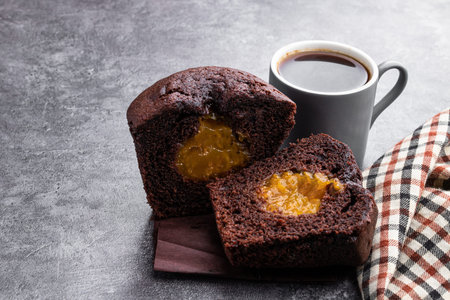 Dark chocolate muffin stuffed with yellow jam and cup of coffee on gray backgroundの写真素材