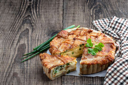 Savory pie with bacon and green onion on wooden tableの写真素材