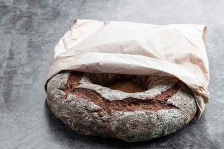 Round freshly baked rye bread in paper bag on gray backgroundの写真素材