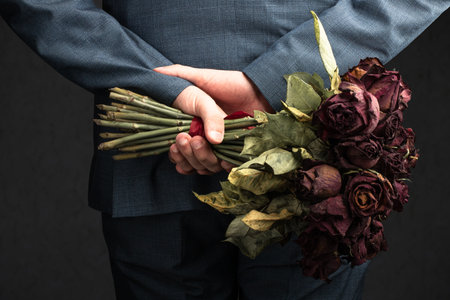 man in suit holding faded roses behind the back conceptの写真素材