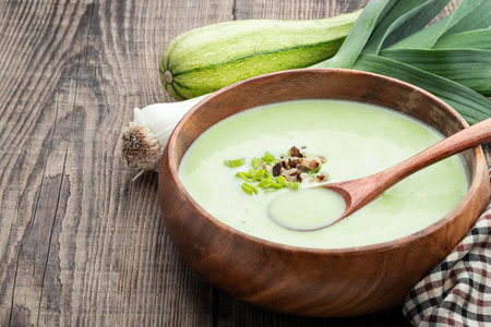 Creamy Zucchini Leek Soup in wooden bowl on rustic tableの写真素材