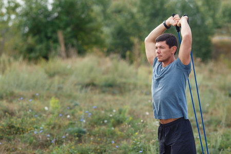 Handsome young muscular sports man exercising outside outdoor with rubber band. Fit, fitness,...