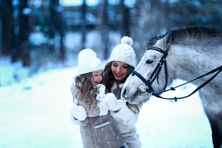 little girl and mom feeding little horse pony winterの写真素材