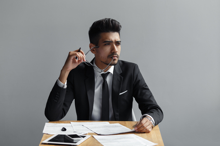 successful man with glasses looking away from the camera, the tablet, telephone and papers on the table.の写真素材